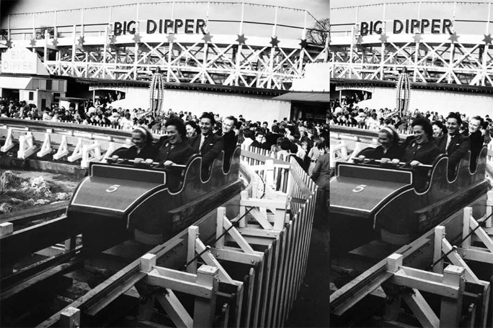 Black-and-white photo of people riding a roller coaster labeled “5” in front of a crowd; a large sign reads “BIG DIPPER” in the background. The scene appears lively and festive.