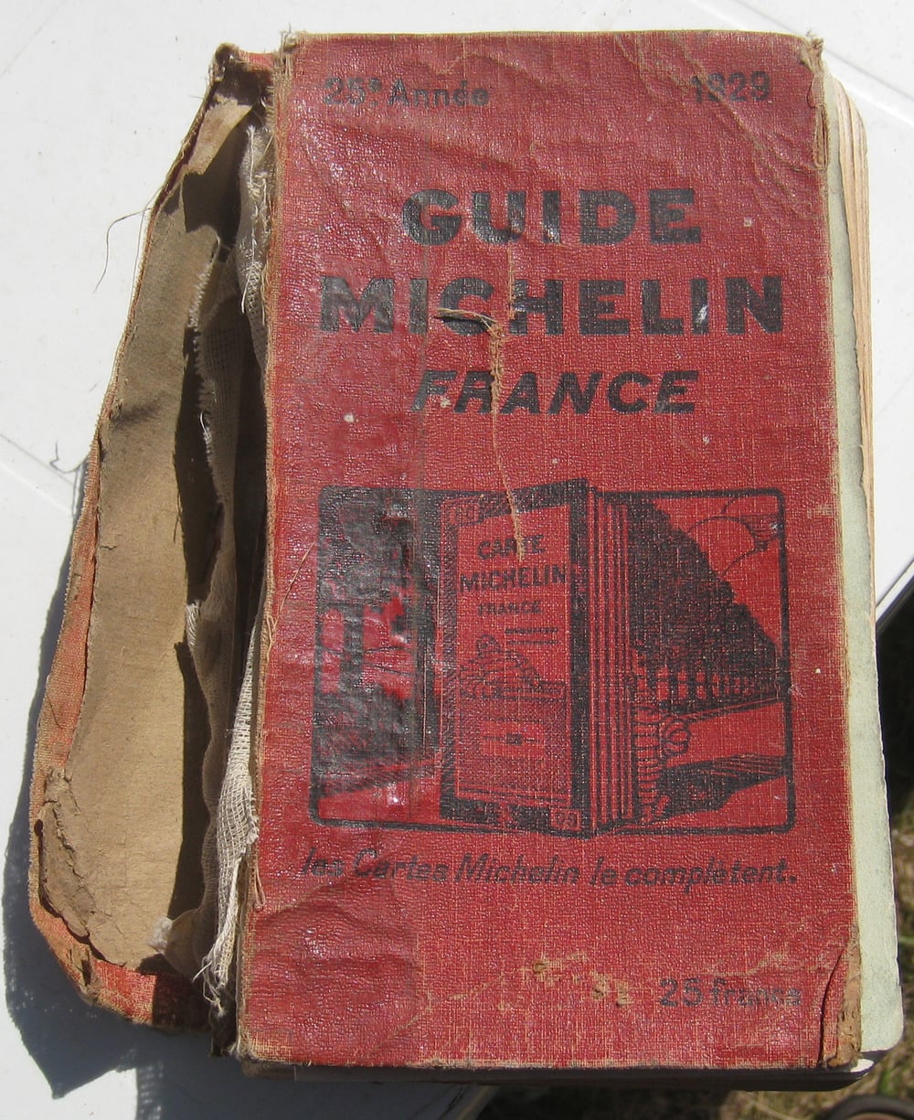 An old, worn red book titled “Guide Michelin France 1929” with a torn spine and faded text sits on a white surface.
