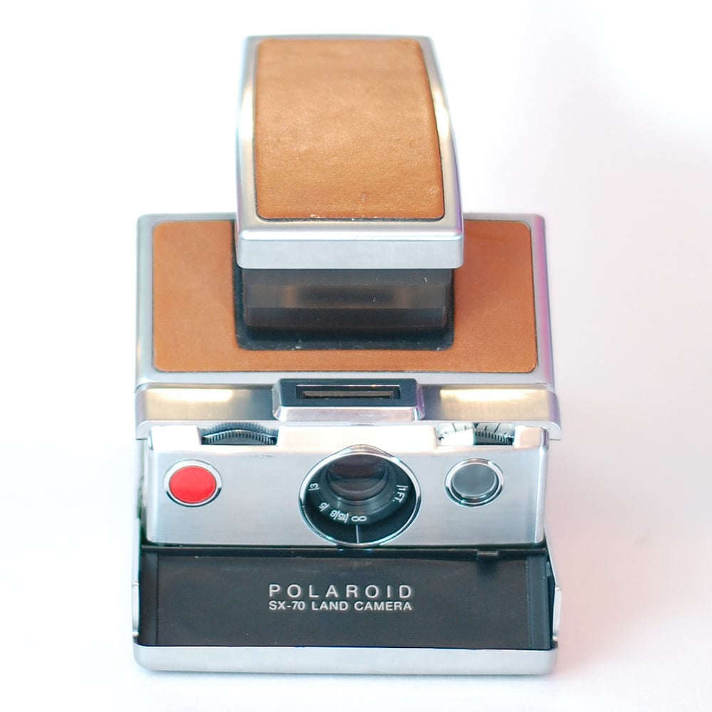 A vintage Polaroid SX-70 Land Camera with brown leather accents is shown against a white background.