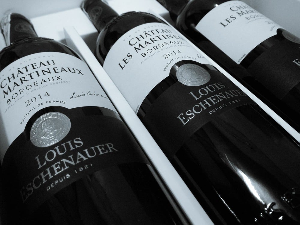 Close-up of three bottles of 2014 Château Les Martineaux Bordeaux wine by Louis Eschenauer, arranged in a white box.