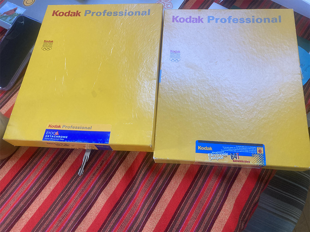 Two large yellow Kodak Professional film boxes sit on a red striped tablecloth; one box is labeled “Ektachrome E100S” and the other “Kodak Ektachrome Duplicating 041.”