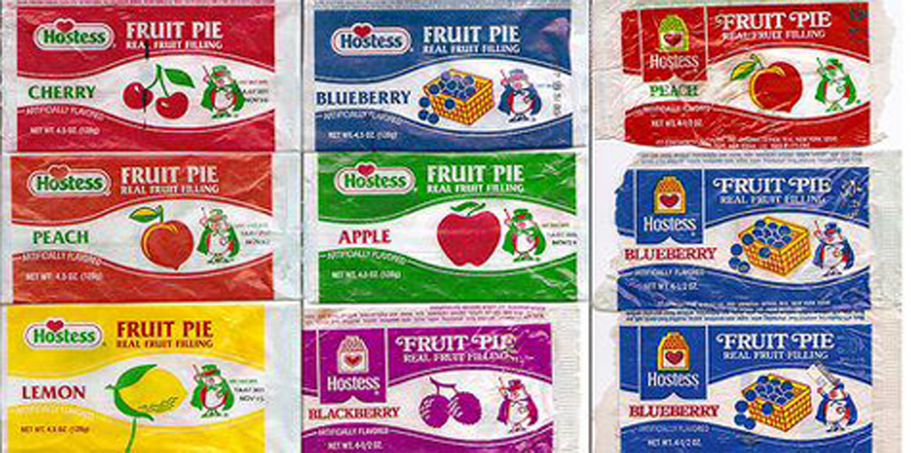 Nine vintage Hostess fruit pie wrappers with cartoon mascots. Flavors shown: cherry, blueberry, peach, apple, lemon, blackberry, and more. Each wrapper features colorful illustrations of the fruits and branding.