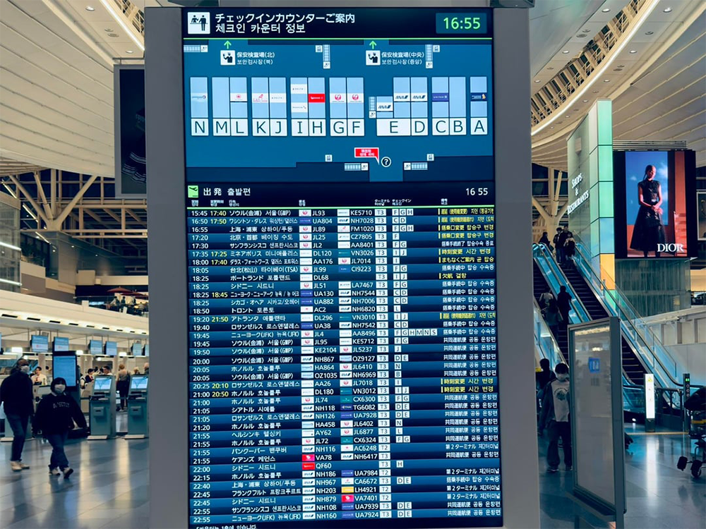 Digital airport departure board shows flight information in English and Korean. Terminal map at top, main hall with travelers and a Dior ad in the background. Time displayed is 16:55.