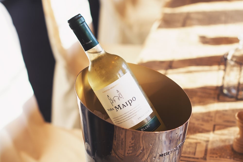 A bottle of Viña Maipo white wine is chilling in a metal ice bucket on a table with a beige patterned tablecloth.