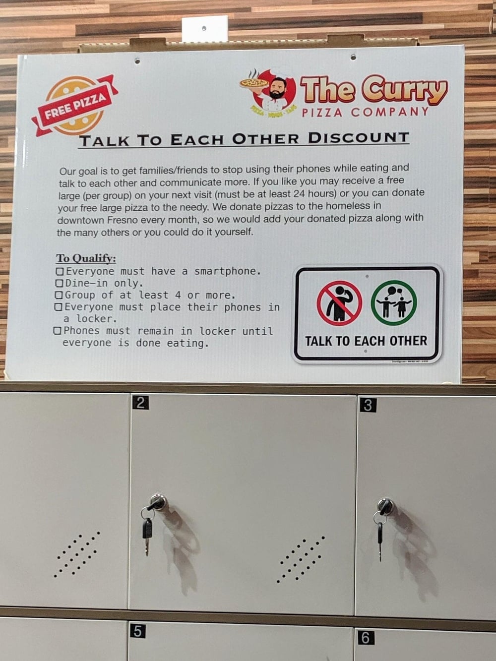 Sign at The Curry Pizza Company explains a “Talk to Each Other” discount for groups putting phones in lockers; reward is free pizza. Lockers with keys are visible below the sign.
