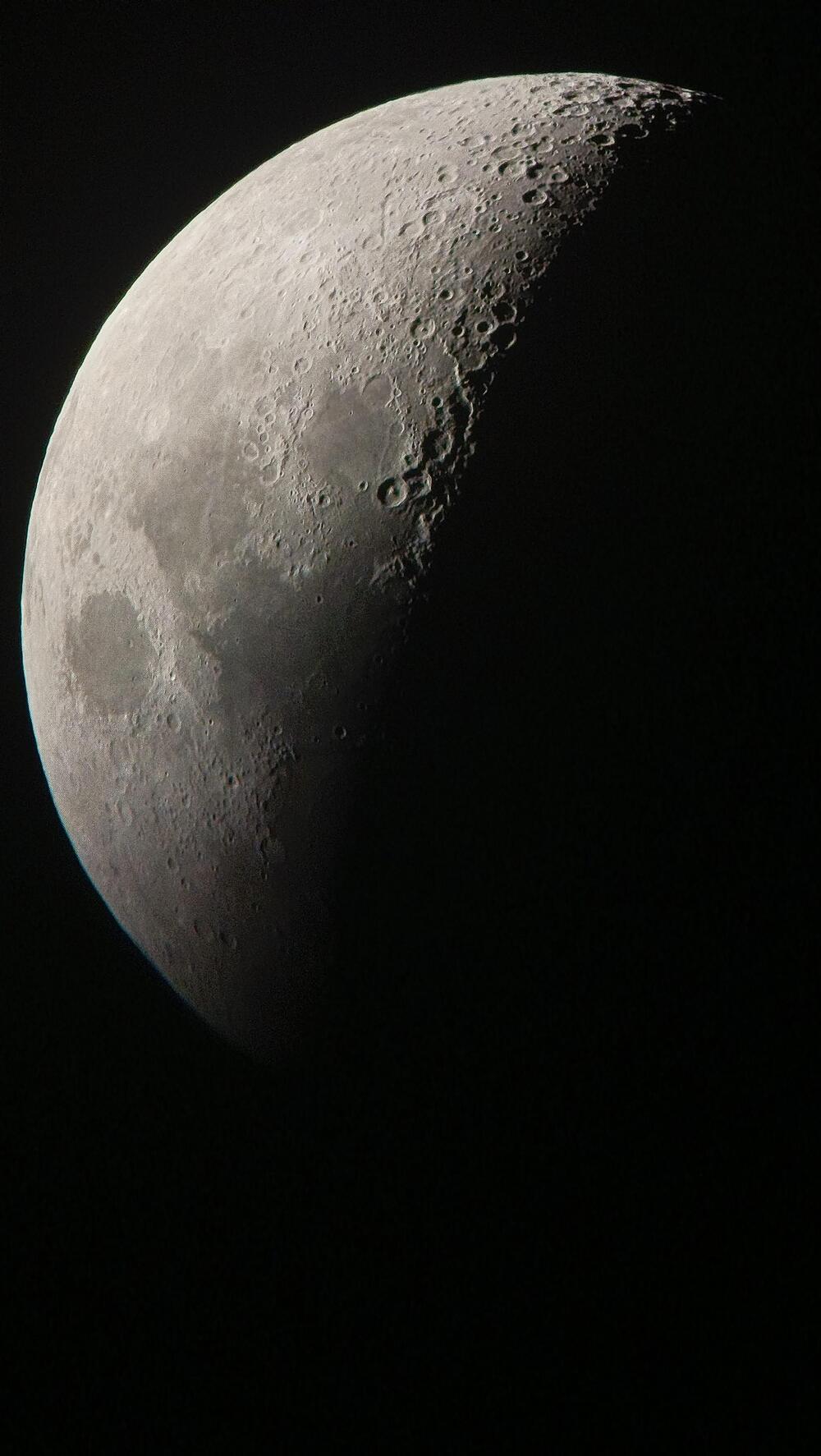 A close-up view of the moon’s surface shows a half-moon phase with detailed craters and rough textures, set against a black background.