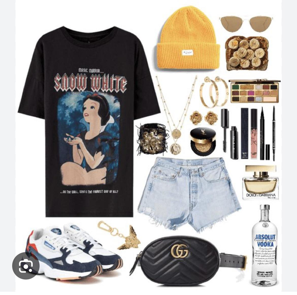 Flat lay of a Snow White graphic tee, denim shorts, sneakers, yellow beanie, sunglasses, gold jewelry, makeup, black belt bag, perfume, vodka bottle, and a box of truffles, all arranged stylishly.
