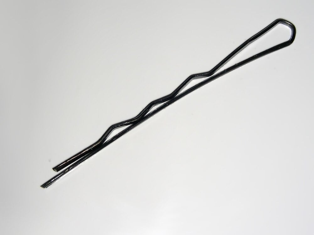 A single black bobby pin with a wavy side and a straight side, placed on a white background.