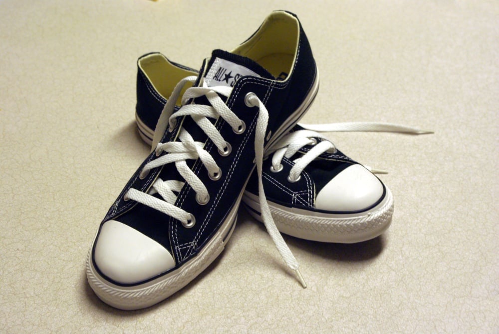 A pair of black and white canvas sneakers with white laces are placed on a light-colored, textured surface.