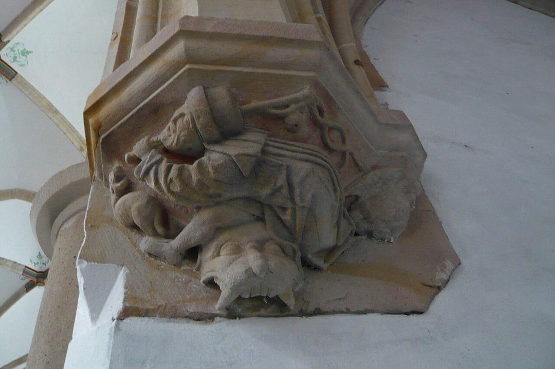 A stone carving on a building shows a person in medieval attire appearing to ride or wrestle with a lion-like creature, with architectural details visible in the background.