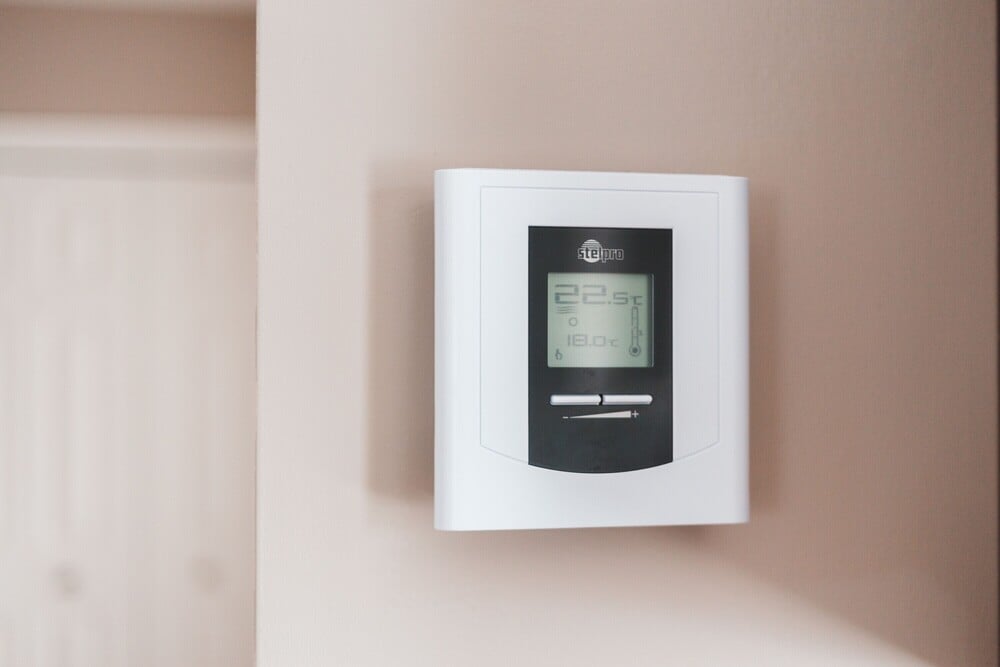 A digital thermostat mounted on a beige wall displays the temperature as 22.5°C. The thermostat has a rectangular screen with simple buttons below it.