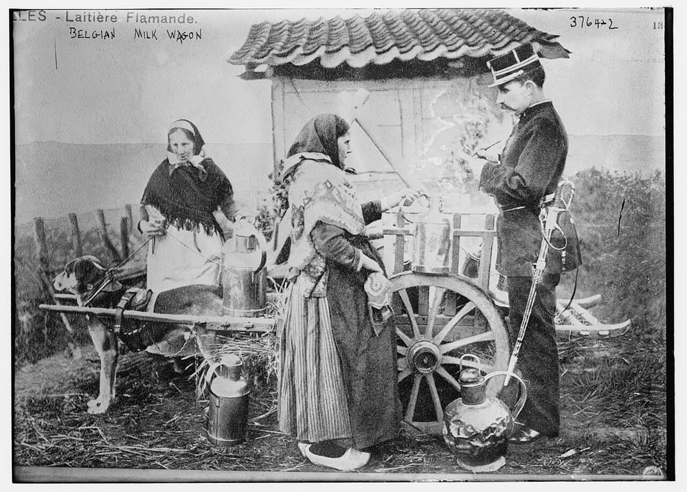 A woman with a milk cart and dog serves a uniformed man while another woman stands nearby. Milk jugs and a building are visible in the background.