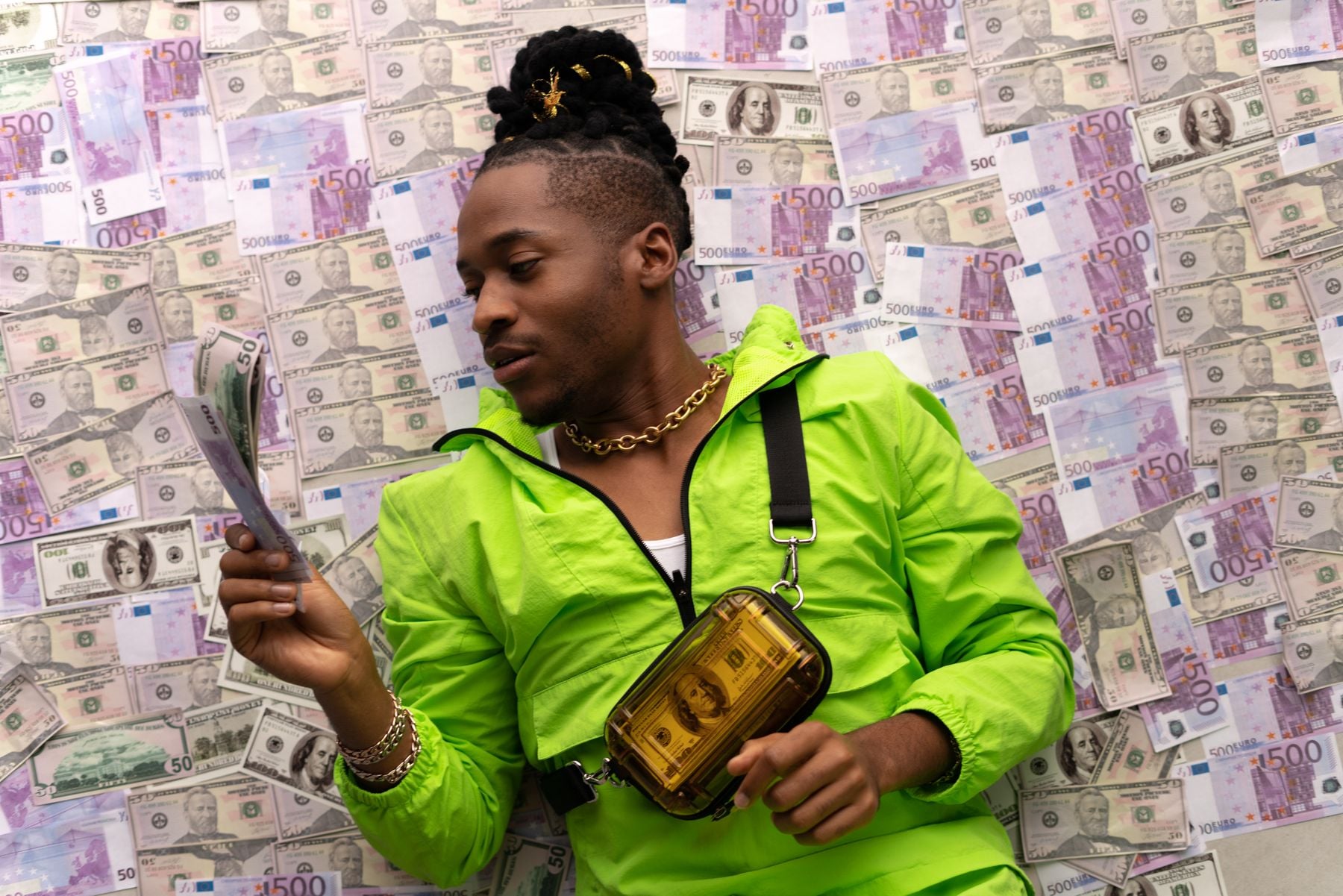 A person in a bright green outfit lies on a floor covered with various currency notes, holding a stack of bills and wearing gold jewelry and a transparent yellow bag.