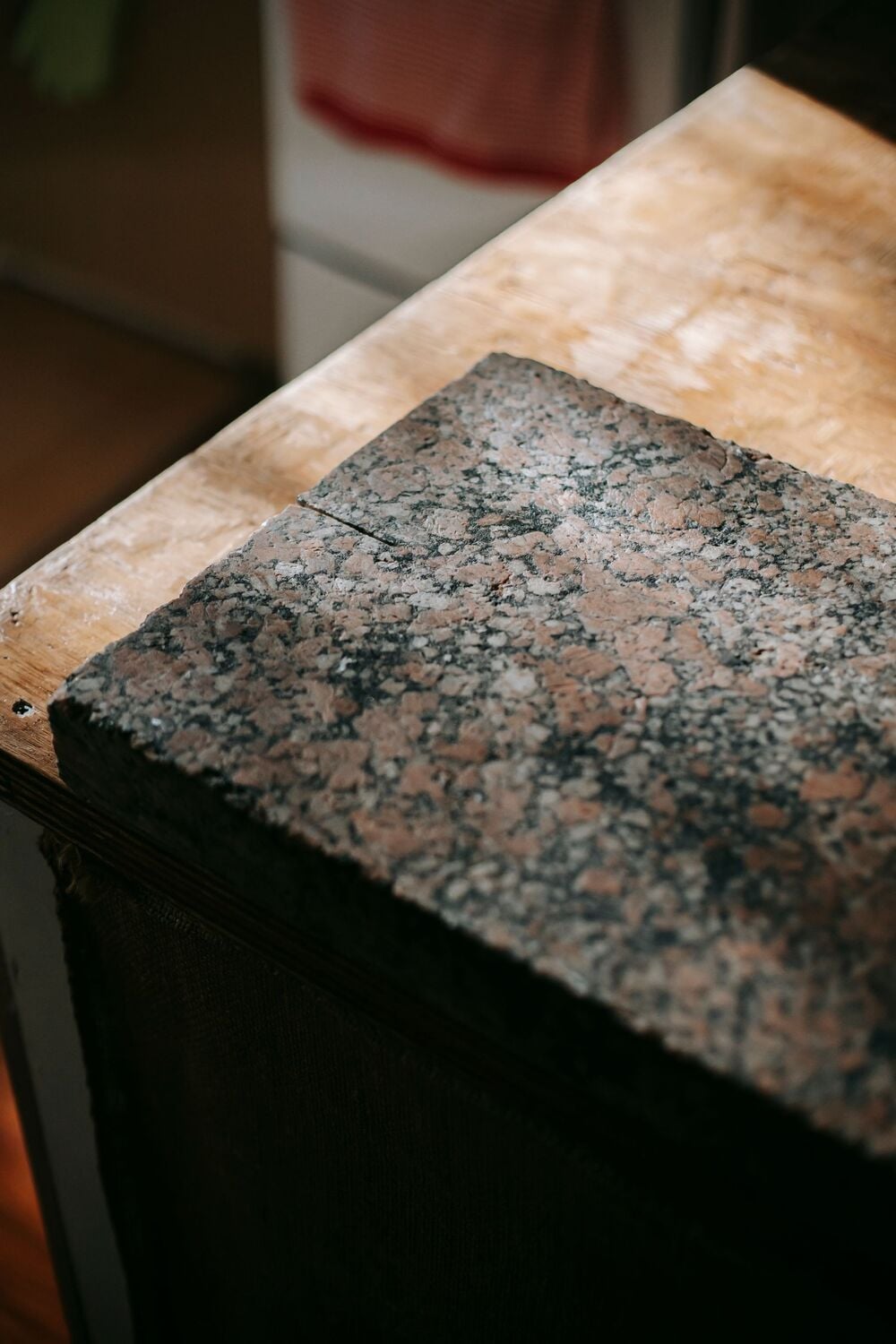 A close-up of a granite countertop slab with a speckled brown and black pattern, resting on a wooden surface in a kitchen setting.