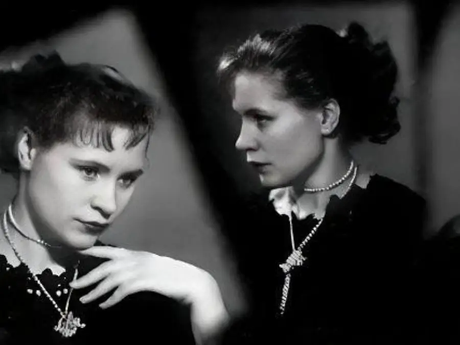 Two women in black dresses with pearl necklaces are shown in a black and white photo. One faces forward with her hand near her collar, while the other is in profile, looking right. Both appear thoughtful and elegant.