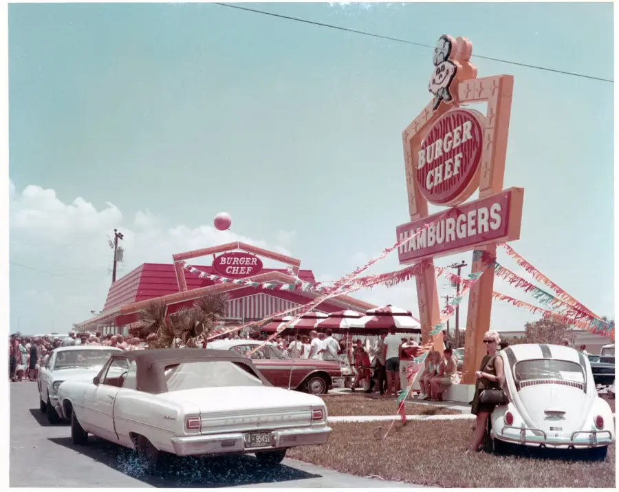 Vintage photo of a busy Burger Chef restaurant, with classic cars parked outside, a large retro sign, and people gathered near the entrance on a sunny day.