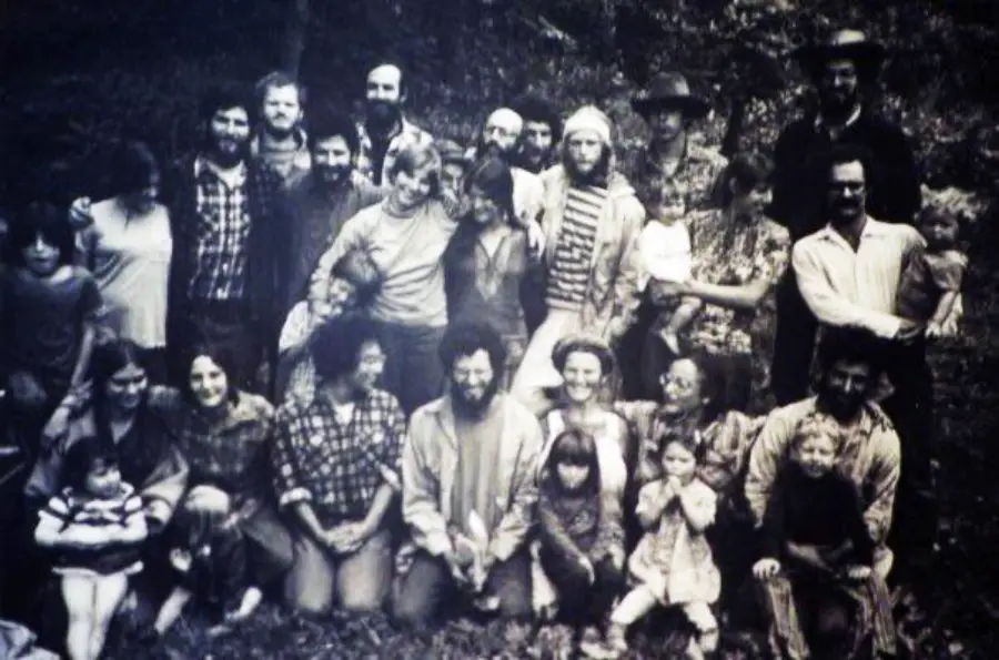 A black-and-white photo of a large group of adults and children posing outdoors, some standing and some kneeling, with trees in the background.