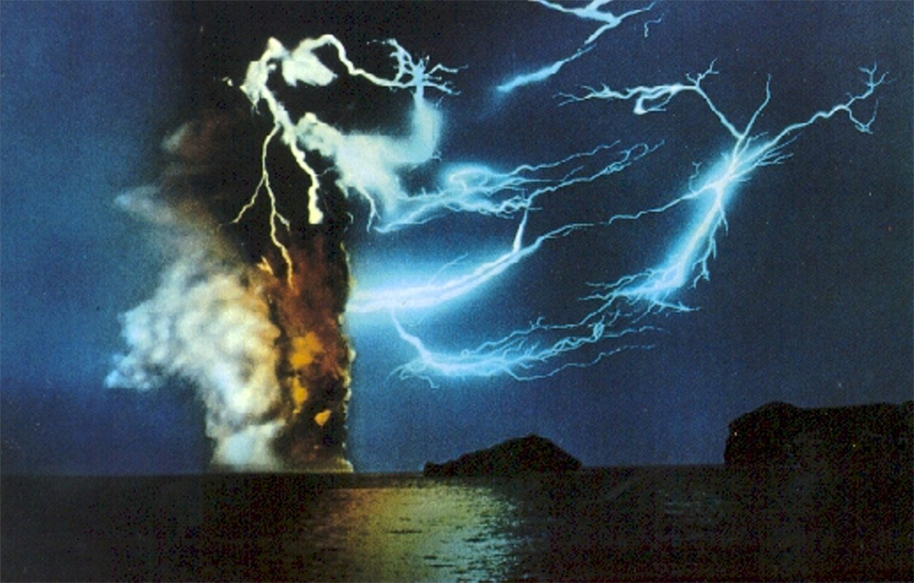 Bright blue lightning bolts streak across a dark night sky above the ocean, illuminating a large, fiery explosion with thick smoke rising and two dark silhouettes of islands in the foreground.