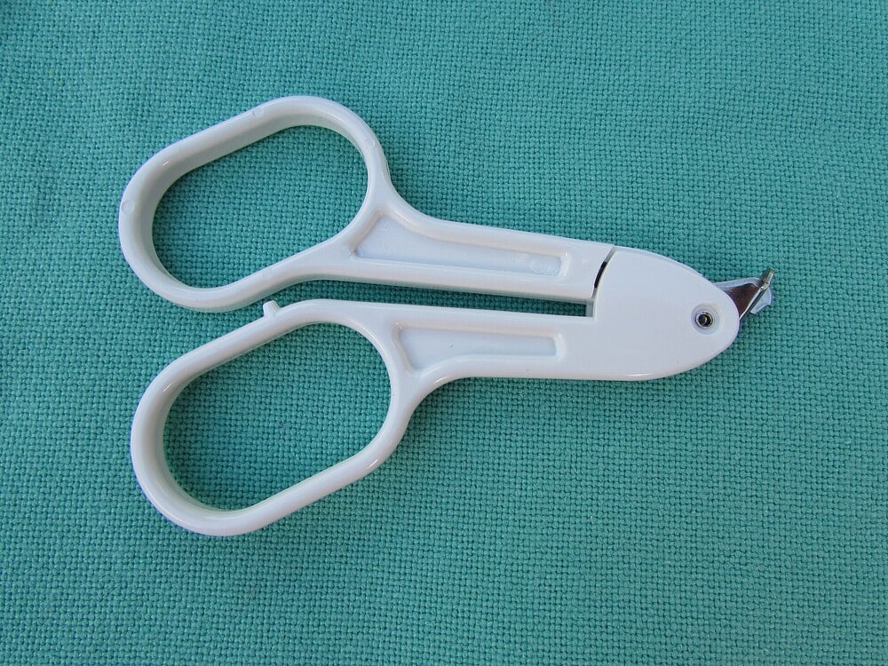 White plastic medical umbilical cord scissors resting on a green textured fabric surface. The scissors have a distinct blunt tip for safety and large handles for easy grip.