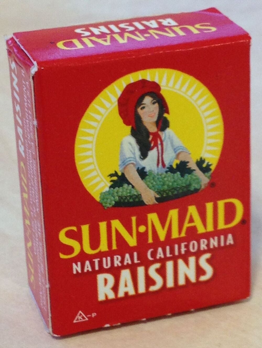 A red box of Sun-Maid Natural California Raisins featuring an illustration of a woman in a red bonnet holding a basket of grapes.