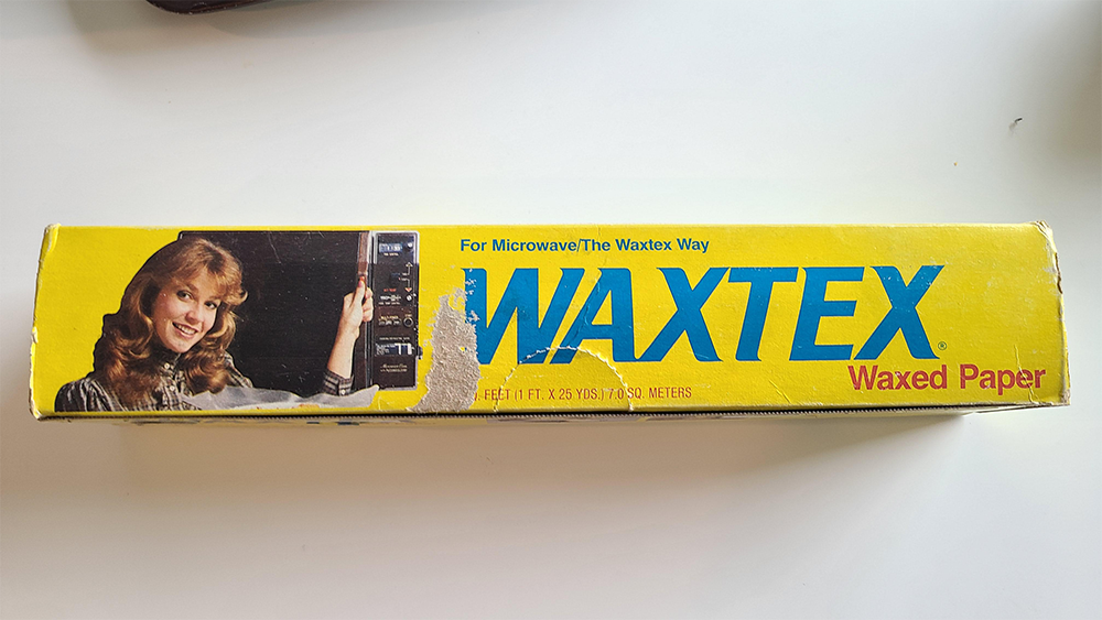 A yellow box of WAXTEX waxed paper with a smiling woman using a microwave. Blue and red text reads “For Microwave The Waxtex Way” and “Waxtex Waxed Paper.” The box is slightly worn.