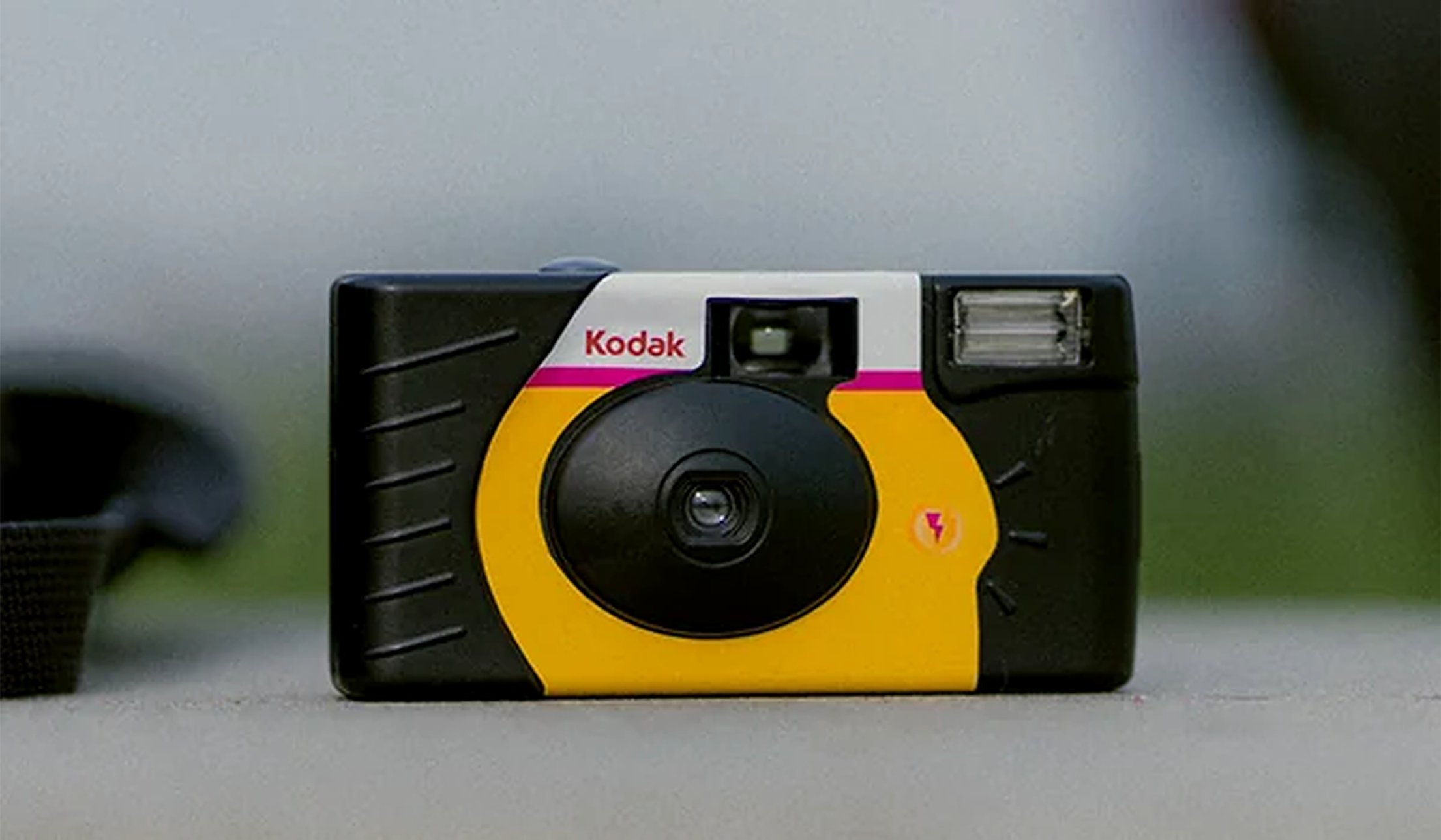 A Kodak disposable film camera with a yellow and black front, lens in the center, flash on the top right, and a Kodak logo above the lens, resting on a flat surface.