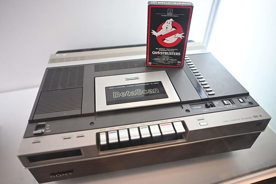 A vintage Sony BetaScan video cassette recorder with a “Ghostbusters” Betamax tape resting on top, displayed on a white surface.