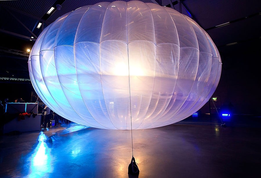 A large, translucent white balloon is displayed indoors under dramatic lighting. The balloon is tethered to the ground and glows from inner illumination, creating reflections on the shiny floor.