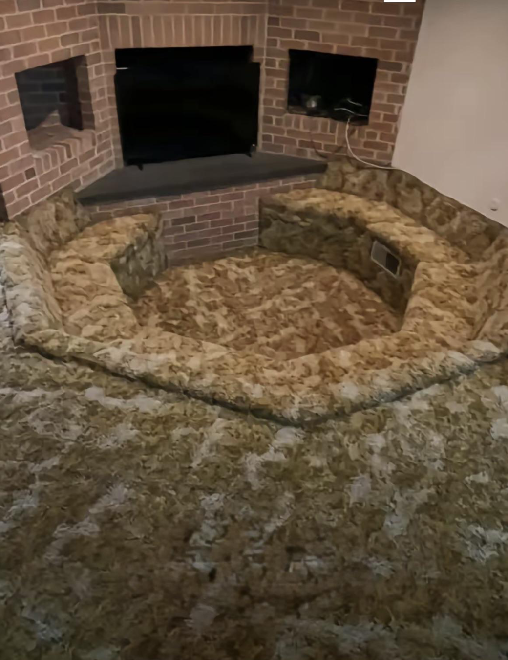 A sunken seating area with carpet matching the floor, surrounded by brick walls and a built-in TV, creating a retro-style living space.
