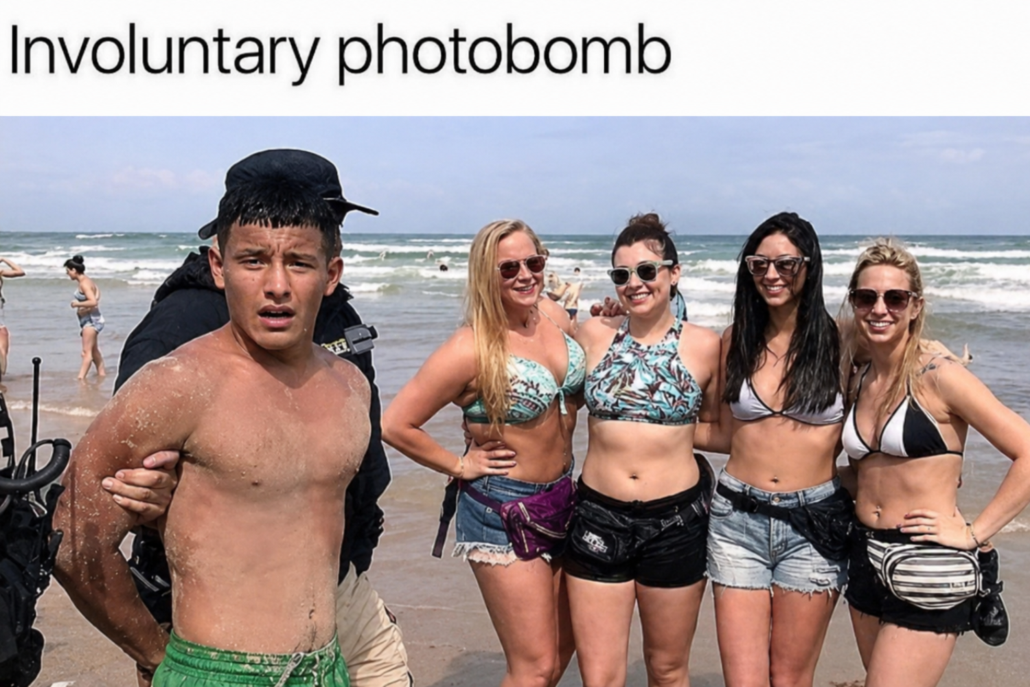 A boy being escorted by police on a beach unintentionally appears in the background of a group photo of four smiling women in swimsuits. The ocean and other beachgoers are visible.
