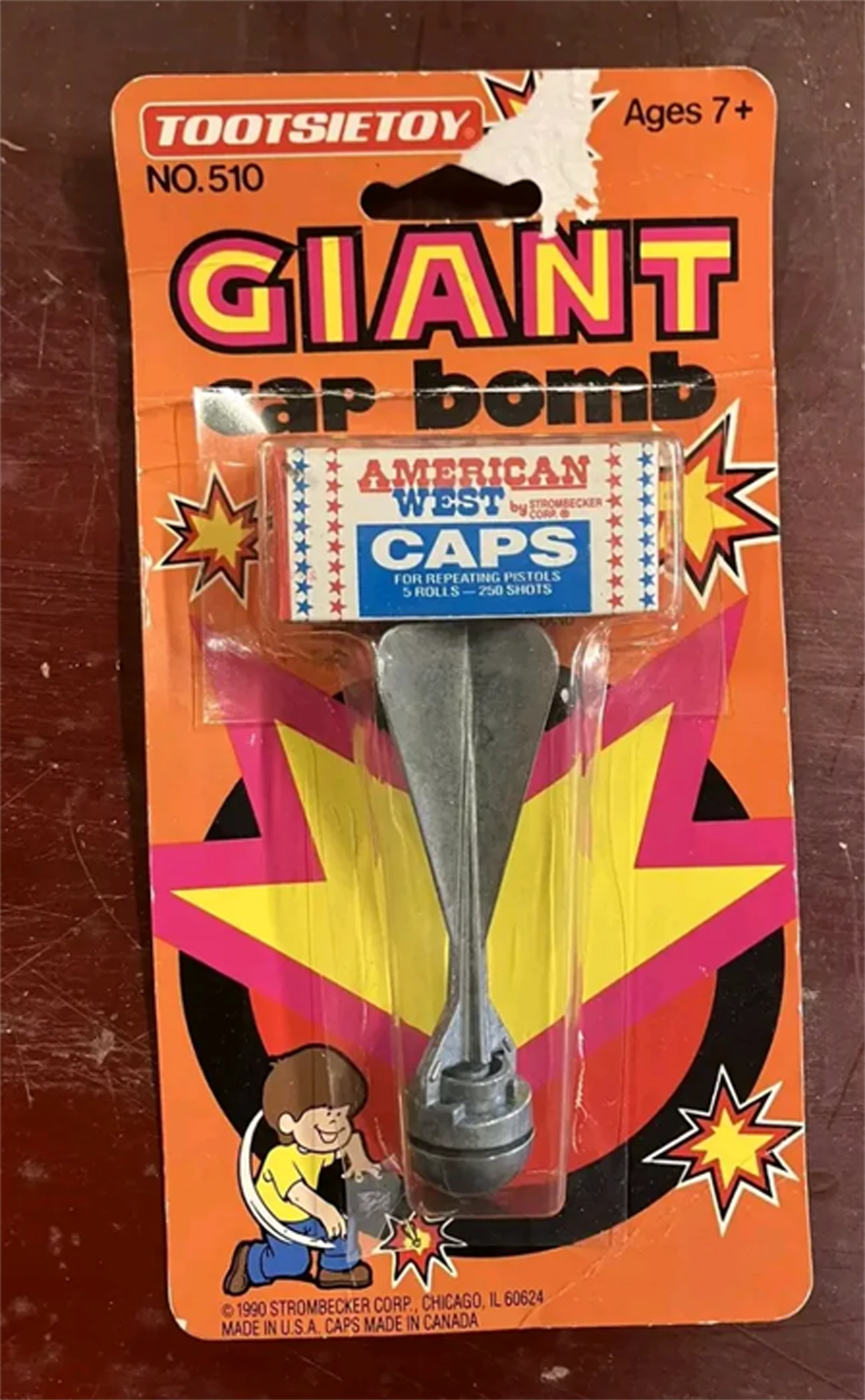 A vintage Tootsietoy “Giant Cap Bomb” toy in original packaging, featuring bright starburst graphics and labeled for ages 7 and up. The toy includes a cap compartment marked “American West CAPS.”