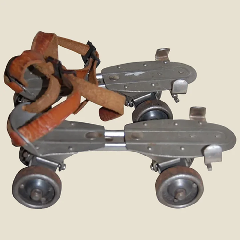 A pair of vintage metal roller skates with brown leather straps and four wheels each, displayed on a plain beige background.