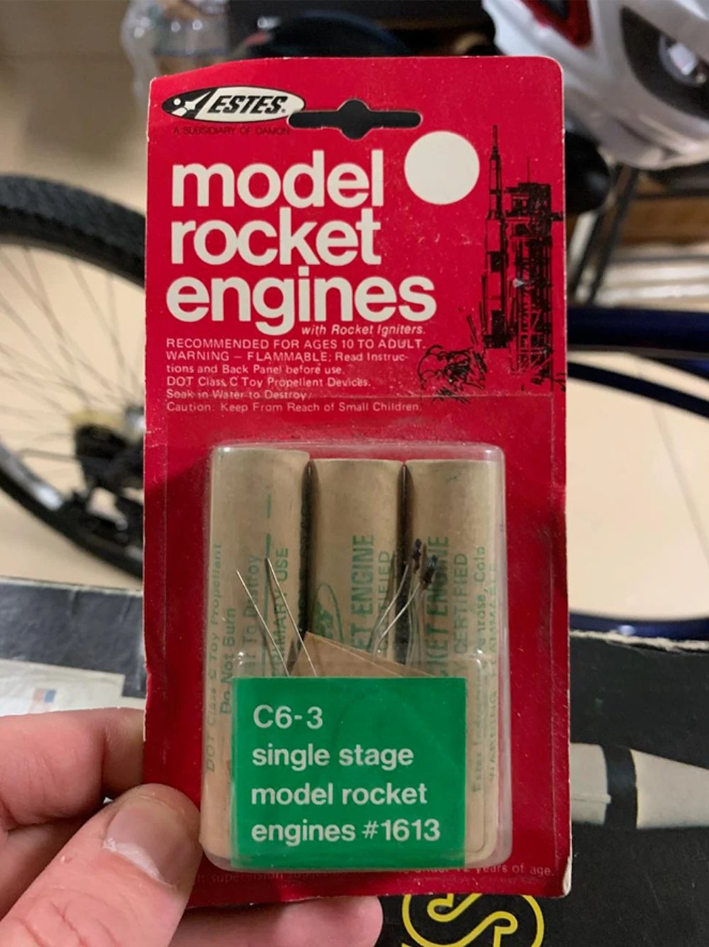 A hand holds a package of Estes model rocket engines labeled “C6-3 single stage model rocket engines #1613” in green, with three engines visible inside clear plastic packaging.