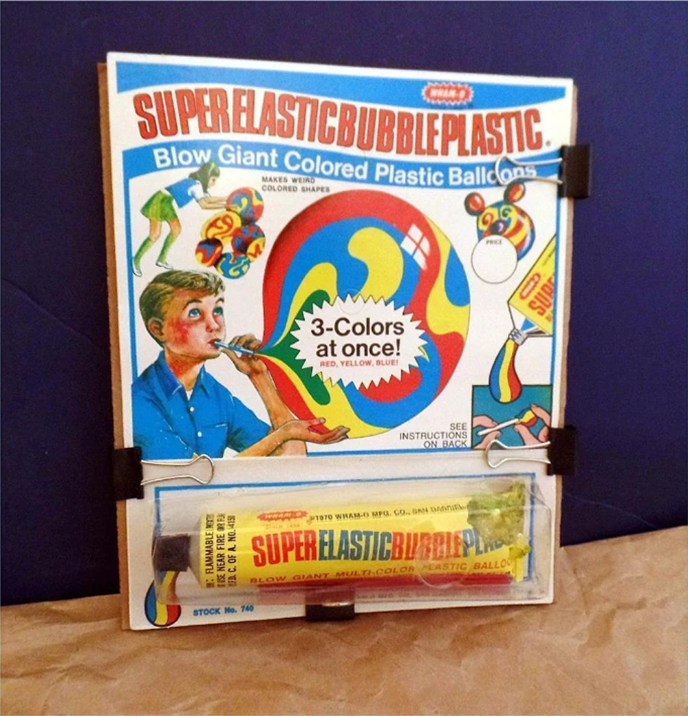 A vintage Super Elastic Bubble Plastic toy package showing a child blowing colorful plastic bubbles and a tube of the product below the illustrated instructions.