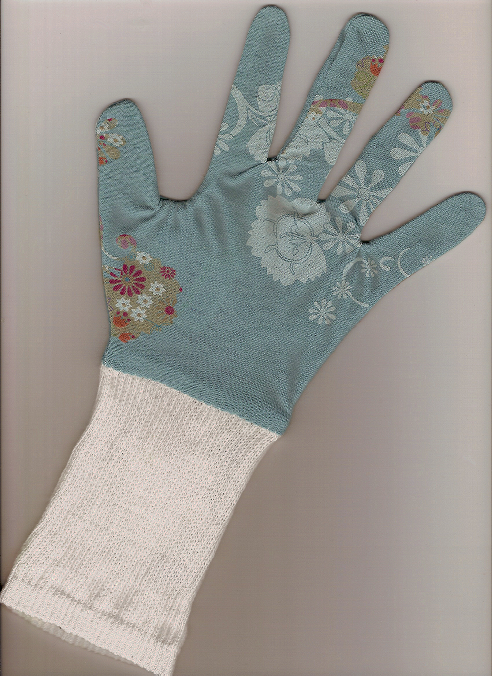 A single blue glove with white floral patterns and a white knit wrist cuff is displayed flat with the palm facing up.