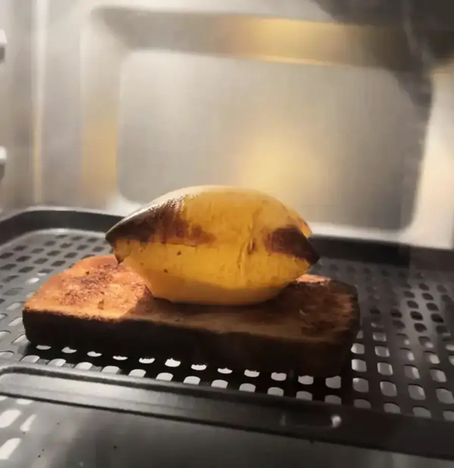 A slice of bread with a partially burnt banana on top sits on a metal rack inside an oven or toaster oven.