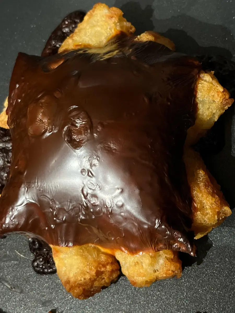A square piece of burnt cheese melted over crispy golden tater tots on a dark surface.