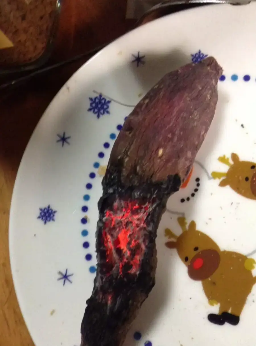 A partially burnt sweet potato with glowing red embers is on a plate decorated with reindeer and snowflakes.