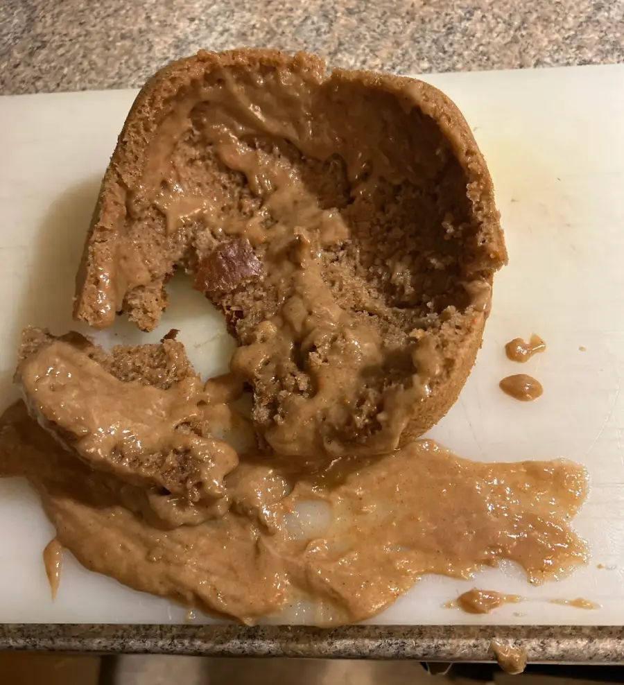 A collapsed, partially liquid chocolate cake sits on a white cutting board, with gooey batter spilling out, suggesting it was undercooked or failed to bake properly.