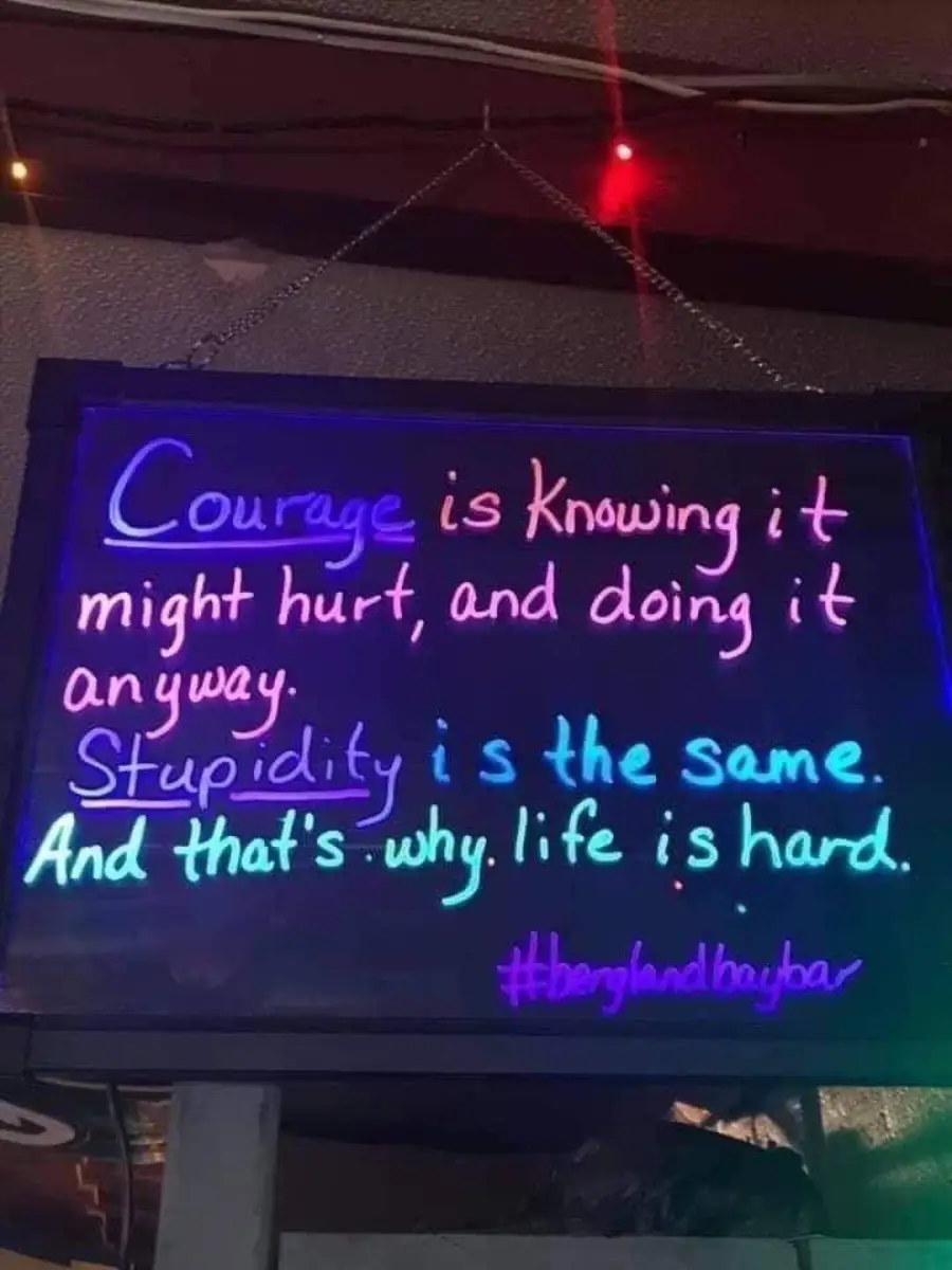 A neon sign reads: “Courage is knowing it might hurt, and doing it anyway. Stupidity is the same. And that’s why life is hard. #banglandbuybar”