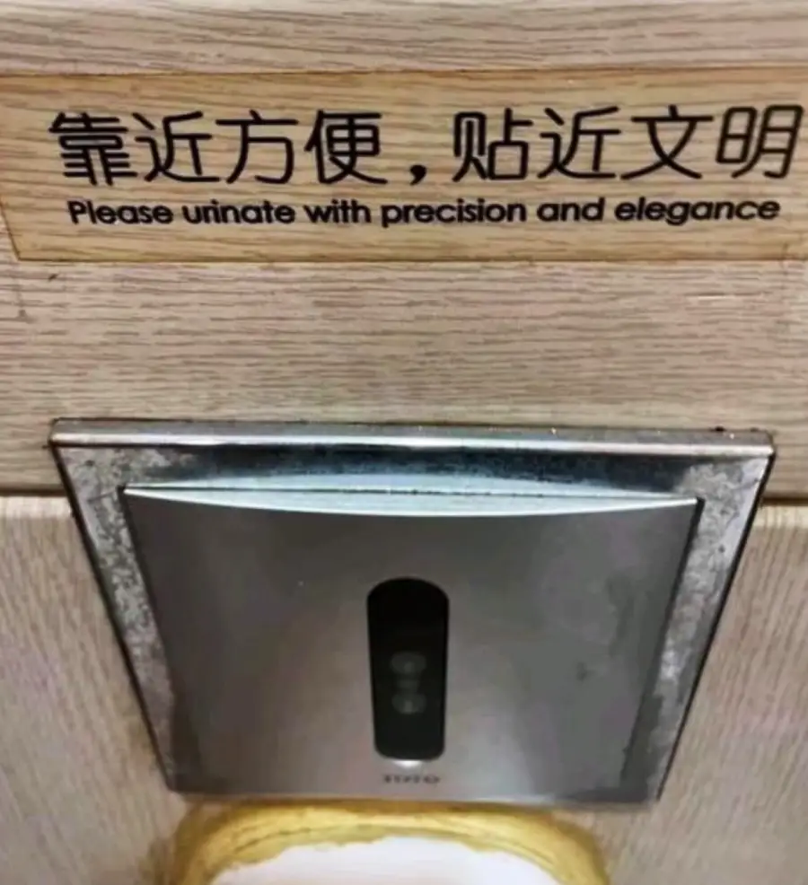 A restroom sign above a toilet sensor reads, “Please urinate with precision and elegance,” in both Chinese and English.