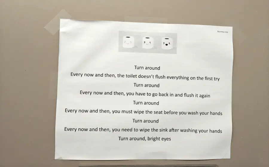 A printed sign taped to a wall shows a humorous poem about toilet etiquette, featuring cartoon toilet paper images at the top and instructions to flush, wipe, and clean after using the restroom.