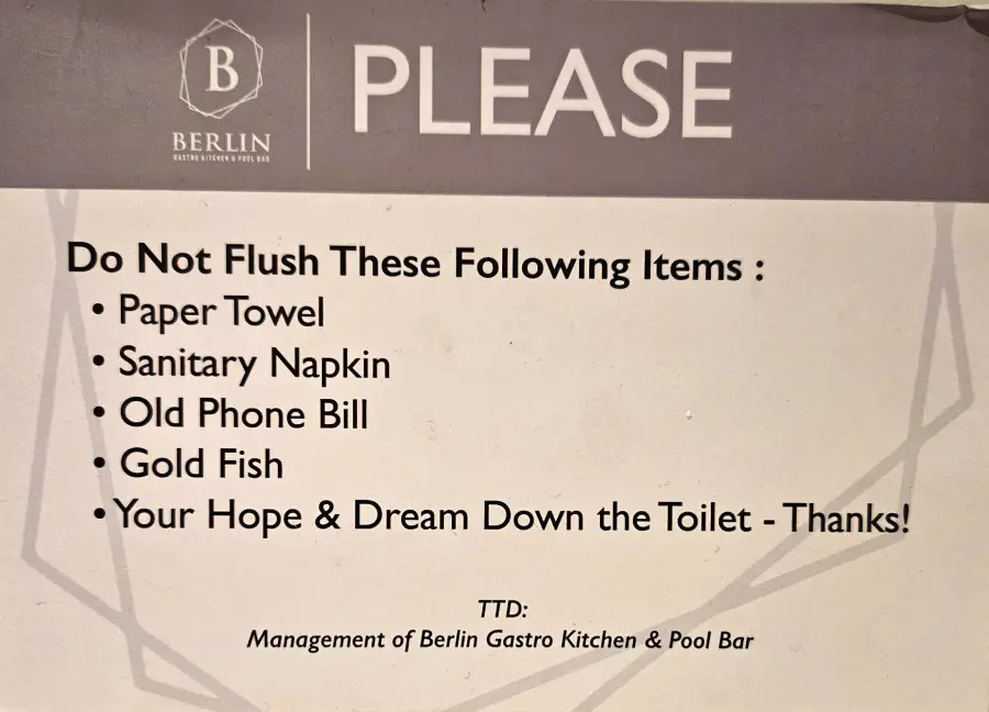 A sign from Berlin Gastro Kitchen & Pool Bar listing items not to flush: paper towel, sanitary napkin, old phone bill, gold fish, and “your hope & dream.” Playful tone.