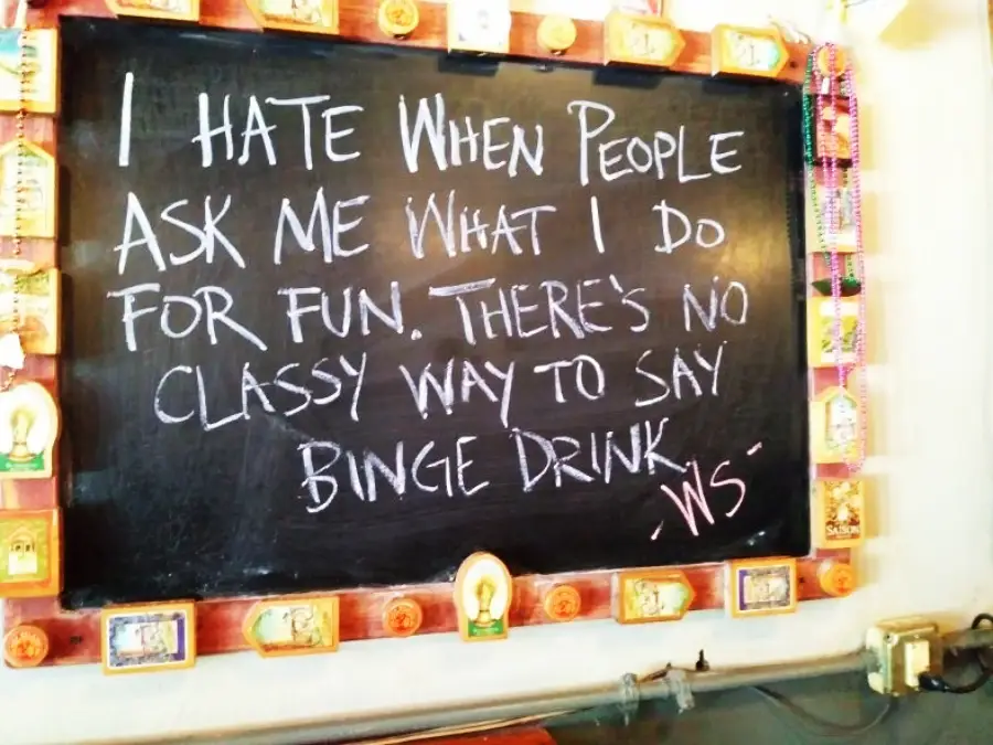 A chalkboard sign reads: “I hate when people ask me what I do for fun. There’s no classy way to say binge drink. - WS” The board is decorated with small pictures and beads.