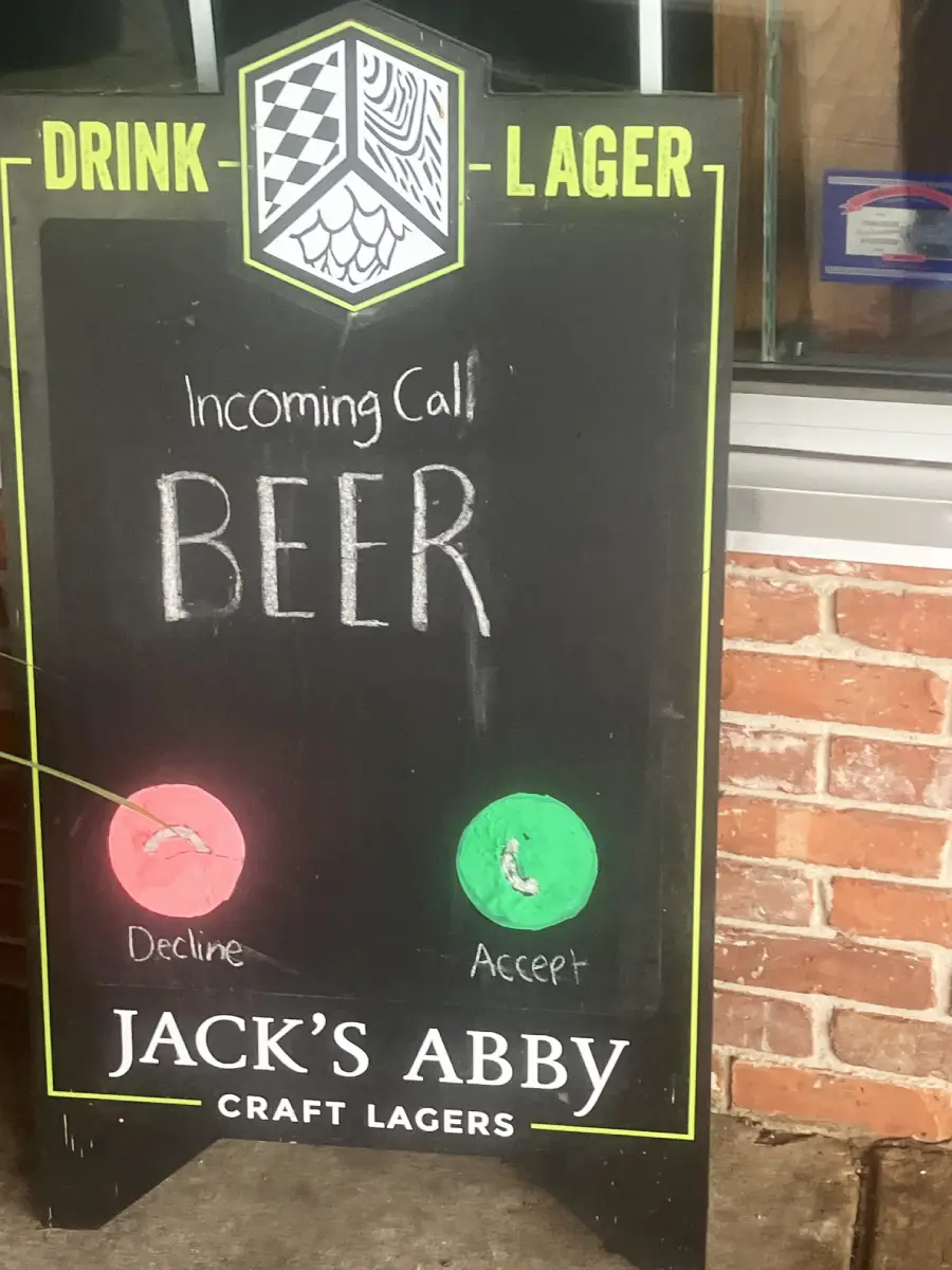 A chalkboard sign reads “Incoming Call: BEER” with red “Decline” and green “Accept” buttons, styled like a phone screen. The sign advertises Jack’s Abby Craft Lagers.
