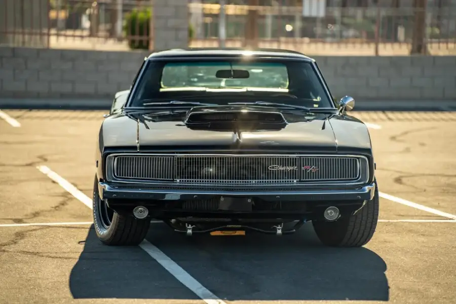 A classic black Chevrolet Camaro RS is parked head-on in an empty parking lot, with sunlight reflecting off its shiny surface.