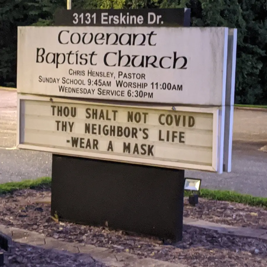 A church sign reads: “Thou shalt not COVID thy neighbor’s life — wear a mask,” urging safety during the pandemic. The church name and service times are listed above.