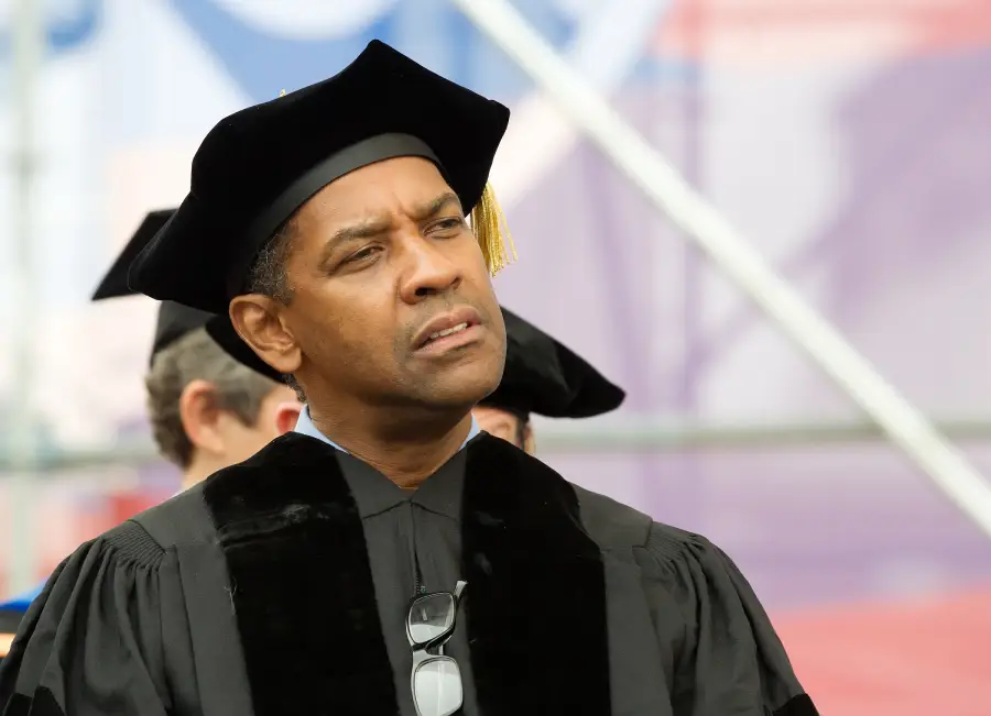 A man in academic regalia, including a black gown and cap with a gold tassel, stands outdoors at a graduation ceremony, looking thoughtful.