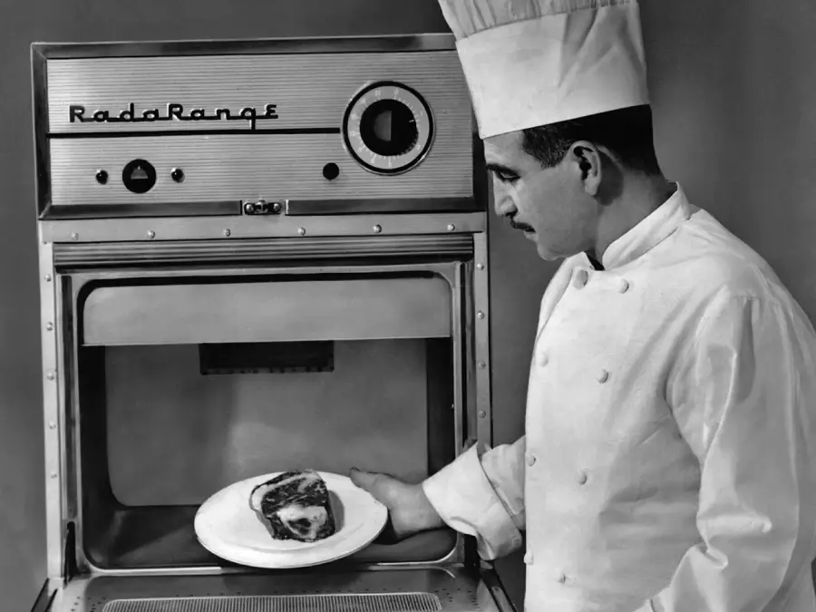 A chef in uniform places a plate with food into an early model microwave oven labeled “Radarange.”
