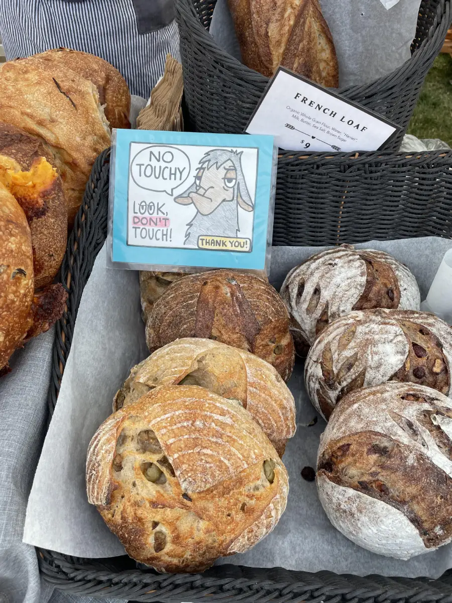 Loaves of artisanal bread in baskets at a market with a sign showing a cartoon llama and the words, “No touchy! Look, don’t touch! Thank you!”